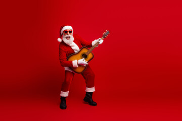 Festive Santa Claus wearing sunglass playing acoustic guitar on a vibrant red background...