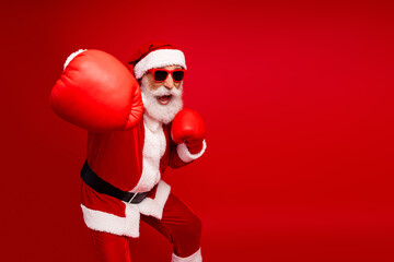 Santa Claus in boxing gloves shows a spirited pose against a festive red background, embodying...