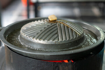 Close-up of Thai-style barbecue grill pan, known as Moo Kratha, with pork belly, shrimp, and vegetables cooking on a hot grill and soup. Popular Asian dining experience in Thailand.