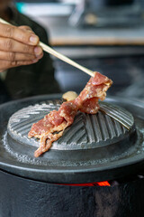 Close-up of Thai-style barbecue grill pan, known as Moo Kratha, with pork belly, shrimp, and vegetables cooking on a hot grill and soup. Popular Asian dining experience in Thailand.