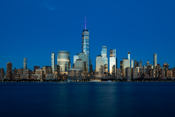 Fototapeta premium A stunning nighttime view of the downtown Manhattan skyline, seen across the Hudson River from Jersey City, with the towers of the Financial District glowing over the dark, tranquil water.