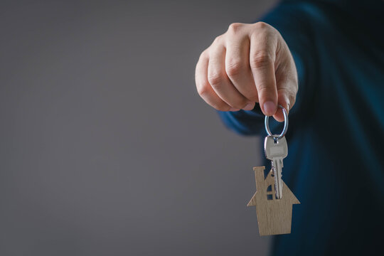 A hand holding a house-shaped keychain and metal key, symbolizing real estate ownership, home buying, property investment, rental agreements, and successful residential transactions.