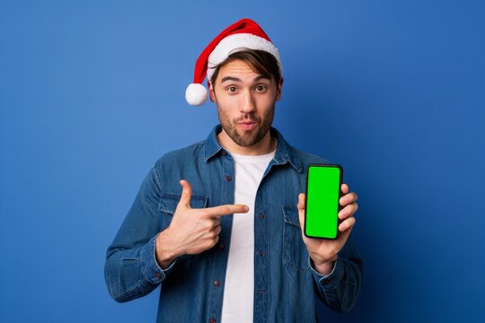 Surprised Man in Santa Hat Points at Phone with Green Screen
