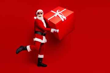 Naklejka premium Santa Claus joyfully holds a giant red gift box against a vibrant festive background, celebrating the essence of Christmas holiday cheer.
