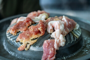Close-up of Thai-style barbecue grill pan, known as Moo Kratha, with pork belly, shrimp, and vegetables cooking on a hot grill and soup. Popular Asian dining experience in Thailand.