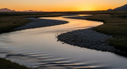 Winding River Reflects Golden Sunset Light Through Grassy Field and Stony Banks
