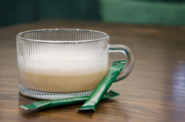 Warm creamy drink served in a transparent ribbed glass mug sits on wooden caf&eacute; table.