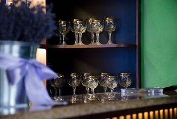 Collection of elegant crystal glasses with gold rims is neatly arranged on wooden shelves in a stylish bar interior.