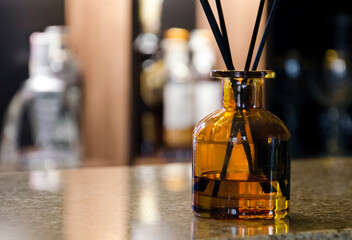 Stylish amber glass aroma diffuser with black reeds stands on a polished bar counter.