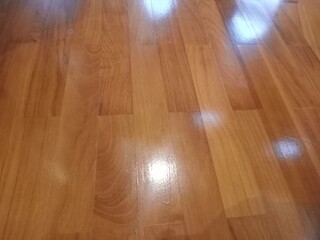 Close-up of a warm brown wooden floor surface with a natural texture and glossy sheen that reflects light. The wood grain details are clearly visible, giving a natural, clean and elegant impression. e
