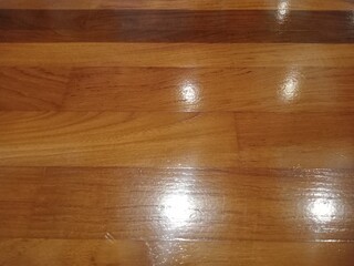 The surface of the wooden floor is glossy with a smooth texture and natural grain pattern, showing a clean and neat warm brown tone. This close-up view is suitable for backgrounds, interior design, od