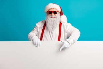 Santa Claus with red suspenders and a fluffy beard smiles behind a blank banner on a bright blue...