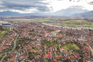 A captivating scene unfolds over Zarnesti, showcasing its charming rooftops nestled in lush greenery. The impressive Piatra Craiului and Bucegi Mountains rise majestically in the distance