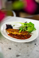 A flavorful chicken kofta kebab served with a side of red beans in sauce, fresh green salad, and a yogurt dip on a white plate. Shallow depth of field food photography