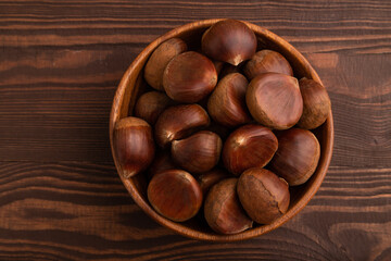 wooden bowl with raw edible Сhestnuts on brown wooden, top view, flat lay, close up, minimalism