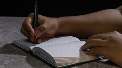 A person?s hands holding a pen and writing on a lined notebook, illuminated with low-key lighting. The scene highlights focus, planning, and personal productivity.
