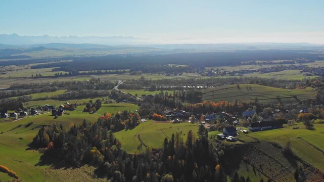 Aerial drone footage of the village of Szlembark on Podhale in Małopolska, with rolling hills, scattered houses and fields, and a distant panoramic view of the Tatra Mountains near Nowy Targ in southe