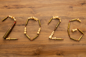 Top-down composition shows cartridges and chess pieces forming “2026” on wood with a nearby magazine; the image reads as a visual forecast combining calendar reference and staged military symbolism.