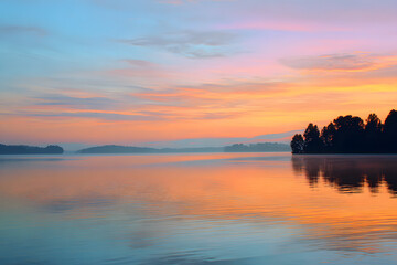 Fototapeta premium sunrise reflecting on a still lake surface with pastel colors creating a peaceful gentle morning calmness