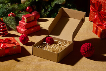A kraft gift box open on a wooden table with red presents and small holiday decorations around it. The scene feels natural and festive, suitable for Christmas e-commerce layouts.