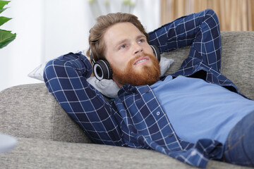 bearded man listening to music relaxing on sofa wearing headphones