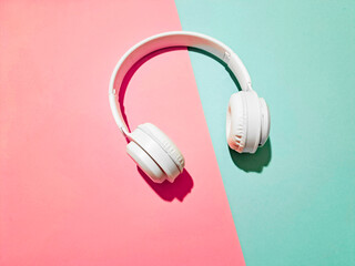 White wireless headphones on pink and blue paper background, copy space