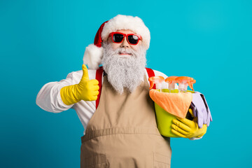 Festive santa with beige apron and yellow gloves holding cleaning supplies and spray bottles while giving a thumbs up