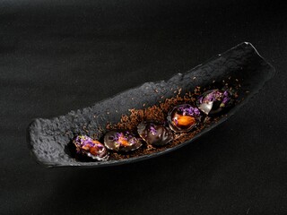 Artisanal chocolate creations are beautifully arranged on a sleek black plate, adorned with colorful edible flowers and delicate cocoa dust