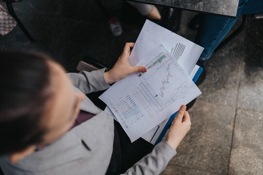 A person in formal attire reviewing financial documents with charts and data, suggesting analysis or decision-making.