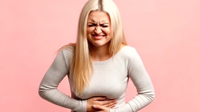 Young woman clutching her stomach in pain, with a distressed expression, against a pink background