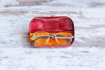 Glasses with gray metal frame and black temples lying in a vintage old plastic case on a wooden background in a minimalist vintage context from the 60s and 70s, close-up.