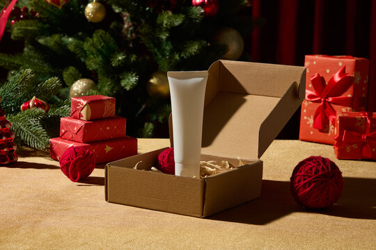 A Christmas table setup with an open cardboard box, red presents, and ornaments near a decorated tree. The warm tones make it fitting for holiday packaging or branding visuals.