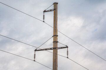 High-voltage power pole with wires against gray sky background, close-up.