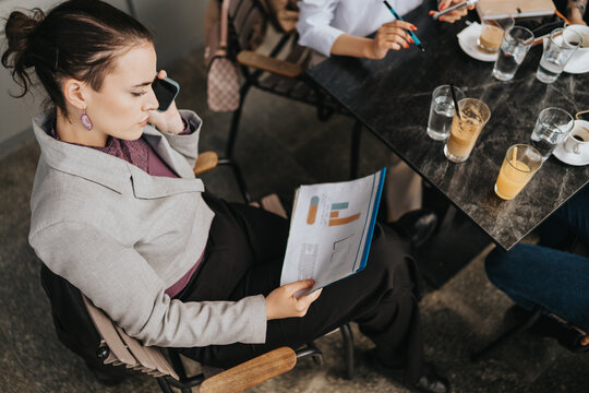 A businesswoman multitasking with a smartphone and data reports during an informal team meeting at a cafe table.