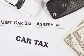 Vehicle sales agreement, car key, white toy car and dollar banknotes. Inscription car tax. Sales, purchases, taxation of automobile. Transportation