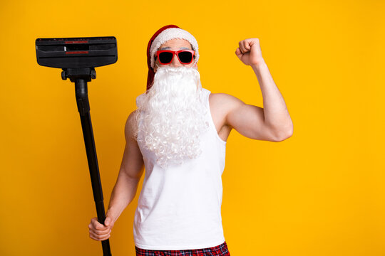 Santa Claus in a bright yellow studio wears beard hat while holding a floor sweeper playful home Christmas perfect family holiday humor campaigns
