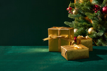 A stack of golden presents arranged neatly beside a Christmas tree on a green table. The lighting creates a refined and elegant festive look.