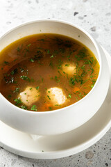 A warm bowl of traditional clear broth soup with floating dumplings, fresh dill, and vegetables.