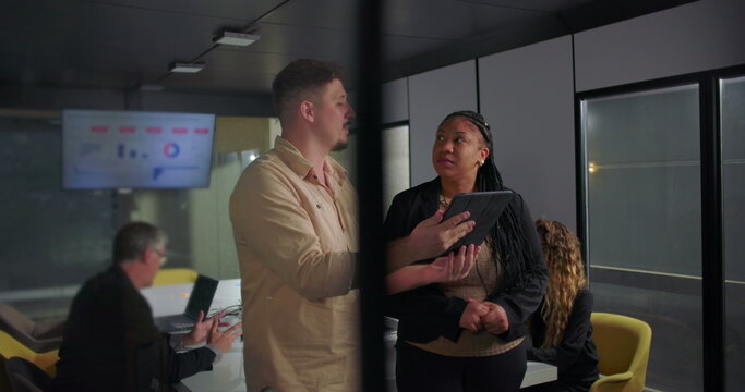 African American businesswoman smiling at digital tablet with young male colleague, collaborative moment in modern office during team meeting - Powered by Adobe