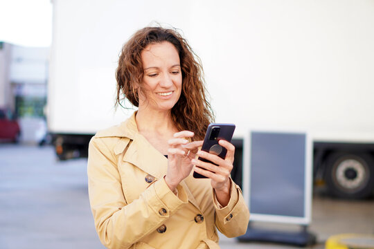 Smiling woman with curly hair checking her cell phone at a gas station. - Powered by Adobe