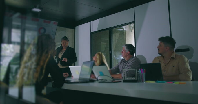 African American businesswoman presenting key data to attentive colleagues during corporate meeting in modern office conference room