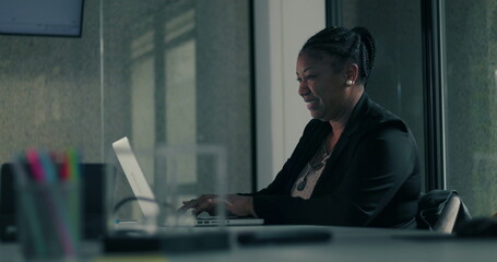 African American businesswoman raising fists in celebration while seated at desk with laptop in modern office