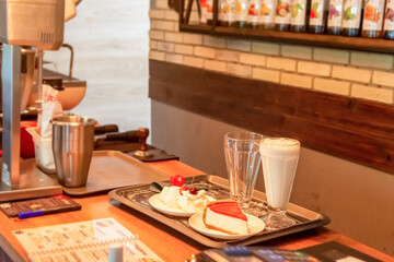 A waiter in a cafe prepares an order of milkshake, cheesecake and ice cream with fruit