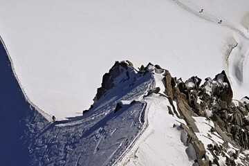 A mountaineer climbs over a snow-covered mountain ridge, Aiguille du Midi, Chamonix-Mont-Blanc, Haute-Savoie, France