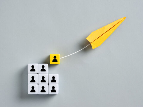 Yellow paper airplane pulling a leader from group of people cubes: concept of headhunting and leadership