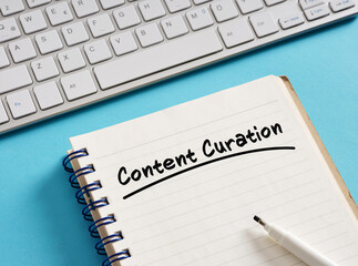 Content curation written on notepad with keyboard and pen on blue background