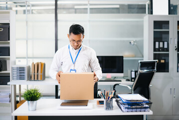 Fototapeta premium Sad Asian businessman packing box in office after job loss or resignation. Perfect for layoff, career change, unemployment, and business stress concepts.