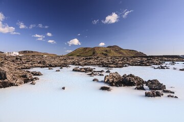 Outdoor thermal pool and geothermal power plant in front of volcanic mountains, Blue Lagoon, summer, sunny, Grindavik, Reykjanes, Iceland