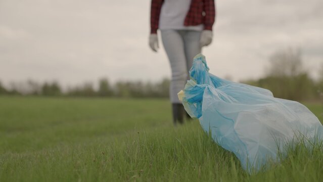 A man carries garbage in garbage bags on green grass, collection and disposal of unnecessary waste, a woman in gloves for cleaning work, help protecting the planet's environment, clean earth.