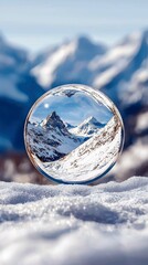 A clear crystal ball sits on a bed of snow, reflecting the majestic, snow-covered mountain peaks and a bright blue sky.